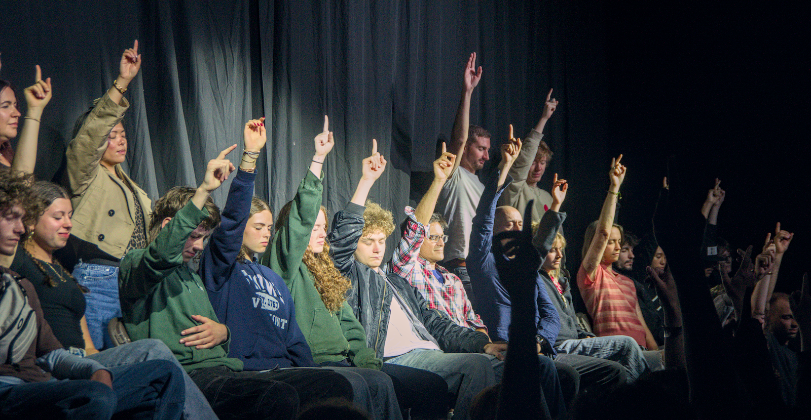 Volunteers raising one hand during a stage hypnosis suggestibility exercise