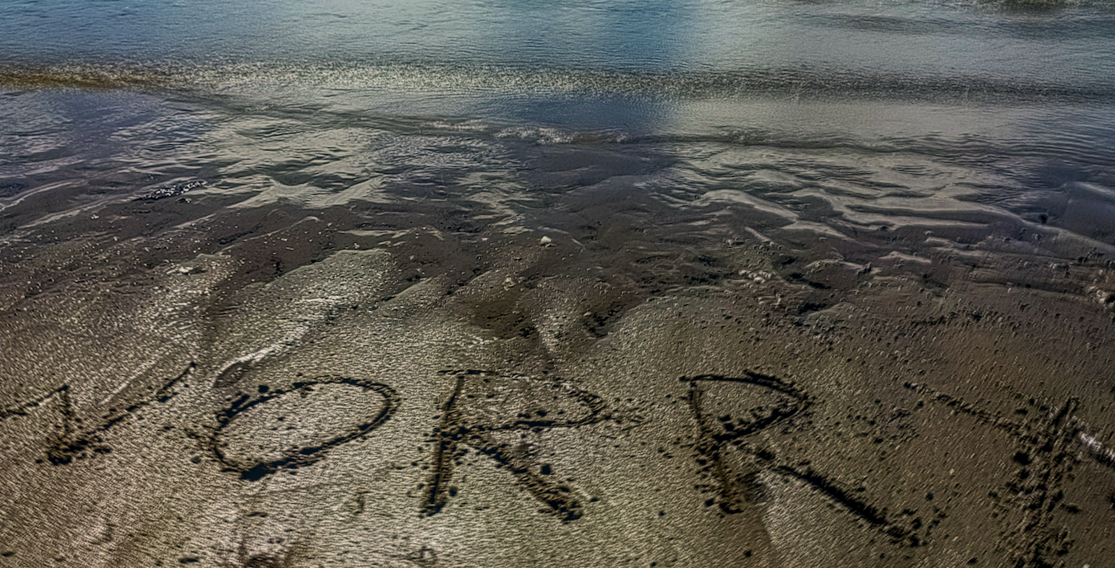 The word “WORRY” scratched into wet sand near the edge of the tide.